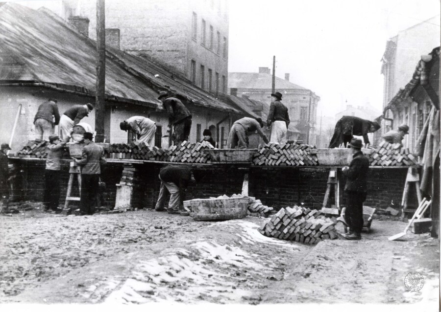 Budowa muru getta (kwiecień-maj 1941 r.) na rogu ul. Krakusa i Piwnej. Kamienica nr 22 (druga po lewej) jako jedyna wśród towarzyszących jej budynków zachowała się do dziś. Fot. ze zbiorów IPN